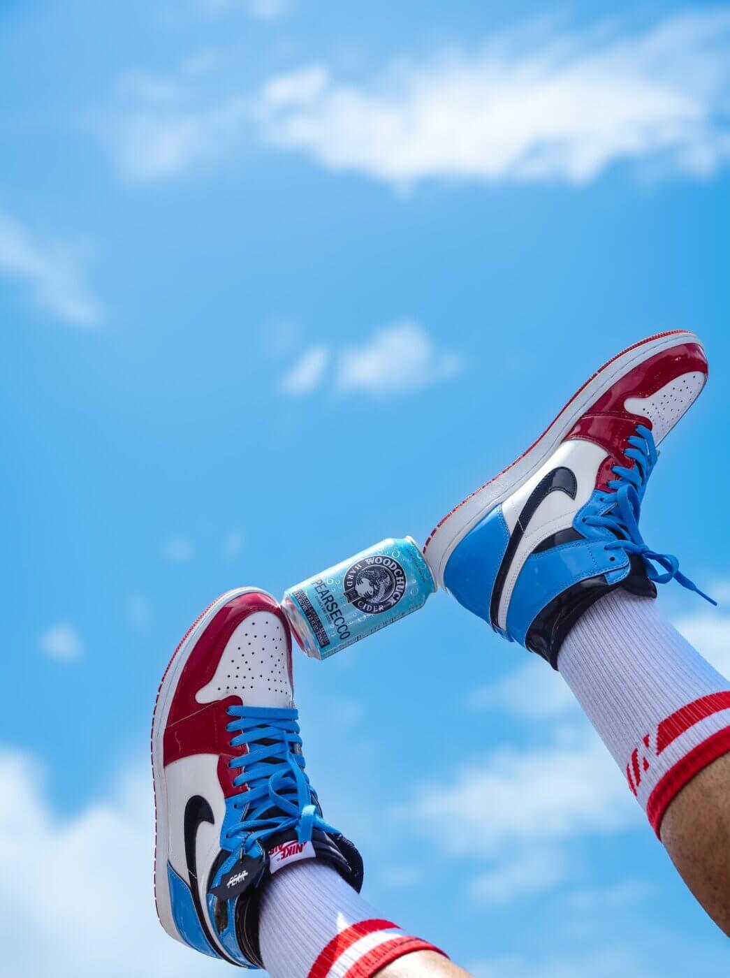 Woodchuck Pearsecco can in the air between two feet with Nike shoes